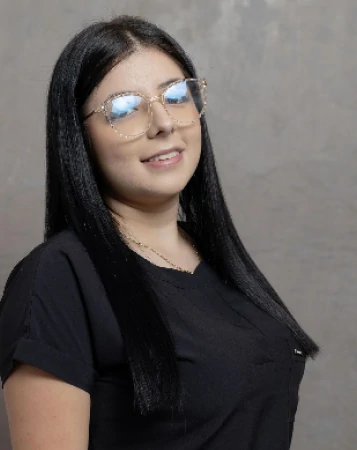 Isabella Díaz con cabello liso negro y gafas transparentes sonriendo ligeramente mientras usa una chaqueta negra